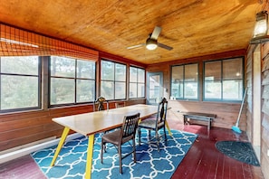 A dining area with a wooden table, chairs, a ceiling fan, large windows, and a broom.
