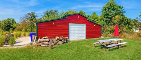 A red barn with a white garage door, a picnic table, and a red umbrella in a grassy yard.