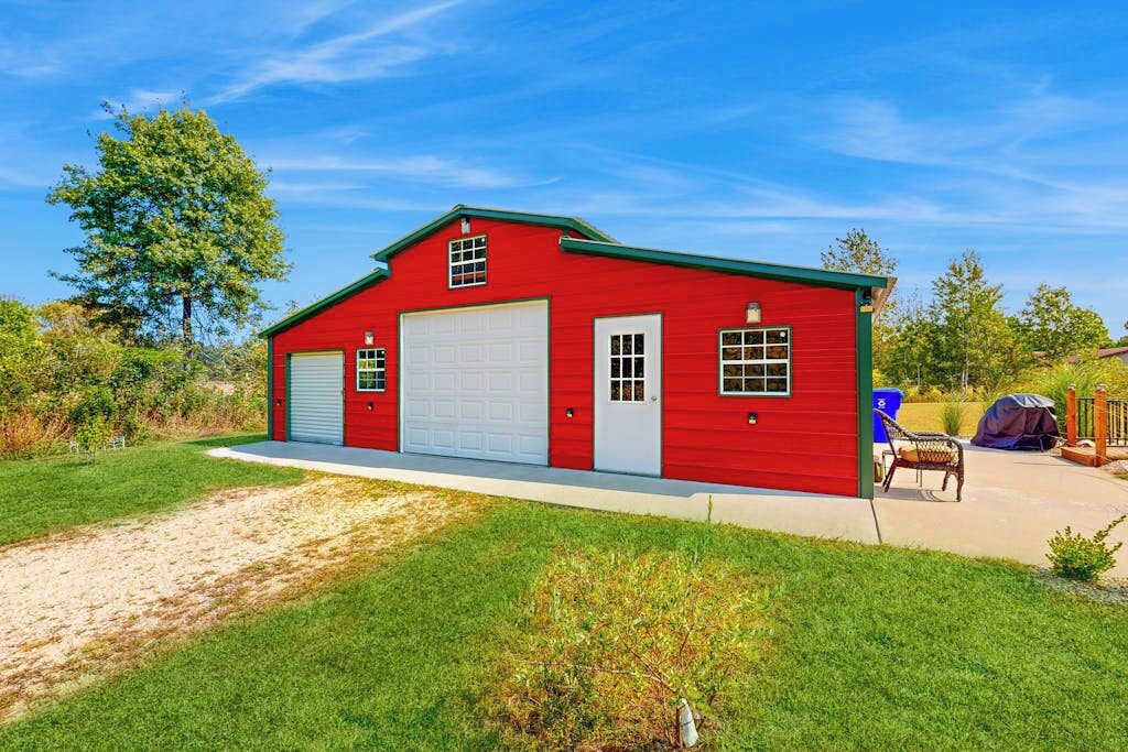 Un edificio rojo de un solo piso con dos puertas de garaje, un pequeño porche y un área de estar al aire libre techada.