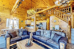 Ein rustikales Blockhaus-Interieur mit einer Holztreppe, einem Essbereich, einer Küche und einem Wohnzimmer mit einer Sofagarnitur.