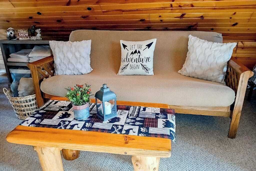 Un divano in legno con due cuscini bianchi, un tavolino decorato e una piccola pianta in vaso.