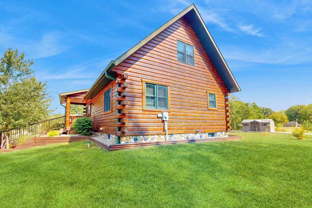 A log cabin with a porch, a small attached shed, and a well-maintained lawn.
