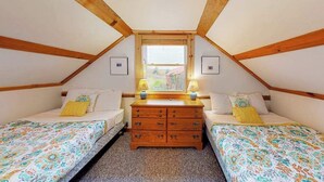A bedroom with two beds, a dresser, and a window.