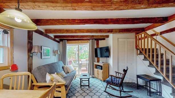 A cozy living room with a sofa, wooden chairs, a table, a TV, and a staircase.