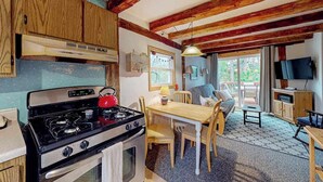 A kitchen with a stove, a dining table with chairs, a television, and a window with curtains.