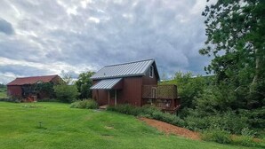 A rustic barn with a metal roof, surrounded by a lush green lawn and dense trees.
