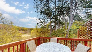 A deck with a round table and two chairs, surrounded by a wooden railing, overlooking a forested area.