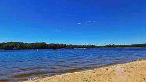 Ein Strand mit klarem, blauem Wasser, einem sandigen Ufer und bewaldeter Küstenlinie im Hintergrund.