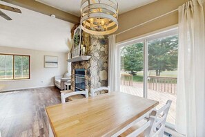 A dining area with a wooden table and chairs, a stone wall, and a large window with a view of greenery. - Cozy Home in Lake Arrowhead w/ shared amenities such as pools, tennis, & golf (Nekoosa)