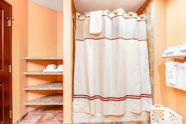 A bathroom with a shower curtain, a towel rack with towels, and a laundry basket. - Spacious Condo & Studio with Jetted Tub & Balcony (Wisconsin Dells)