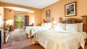 Quarto de hotel com duas camas, uma mesa, uma cadeira, uma TV e varanda com vista.