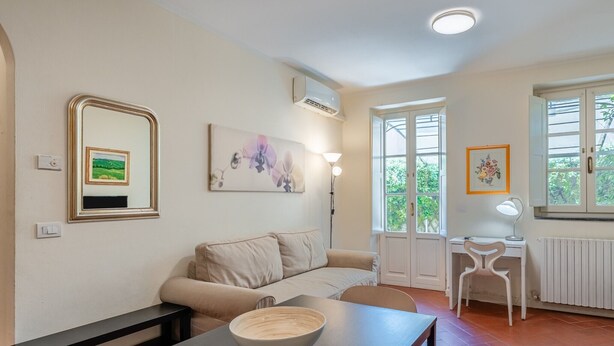 Ein Wohnzimmer mit Sofa, Tisch mit Schale, Schreibtisch mit Stuhl und Fenster mit Ausblick.