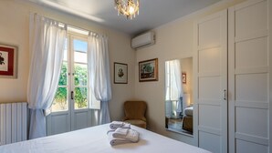 Ein Hotelzimmer mit Bett, einem Sessel, einem Fenster mit Vorhängen, einem Spiegel und einer Wand-Klimaanlage.