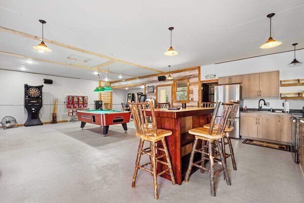 A spacious room with a pool table, bar area, and kitchen.
