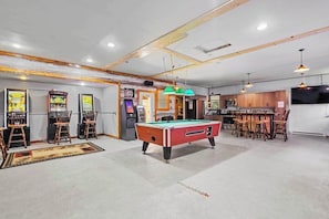 A pool table in a room with arcade games, a bar area, and a television.