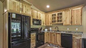 A kitchen with wooden cabinets, a black refrigerator, a microwave, an oven, a dishwasher, and a granite countertop. - Contemporary dog-friendly cabins with hot tub, fireplaces, patios, & game room (Conover)
