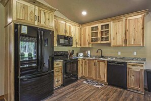 Une cuisine avec des meubles en bois, un réfrigérateur noir, un four à micro-ondes, un four traditionnel, un lave-vaisselle et un plan de travail en granit.