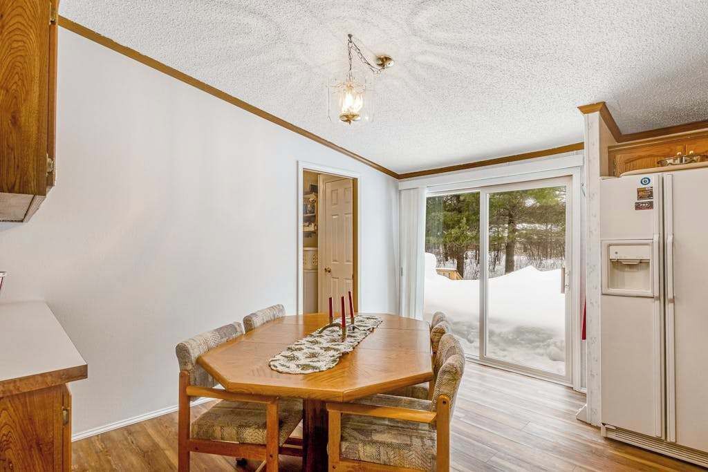 Un coin repas avec une table et des chaises en bois, un luminaire au plafond et une vue sur l’extérieur par une porte vitrée.