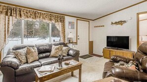 Ein Wohnzimmer mit Ledersofa, Couchtisch, Fernseher auf Holzfuß und einem Fenster mit Vorhängen.