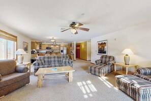 A spacious living area with a sofa set, a coffee table, a dining table, and a kitchen in the background.