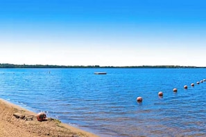 Ein Strand mit klarem, blauem Wasser, einem sandigen Ufer und einer Reihe von schwimmenden Bojen.