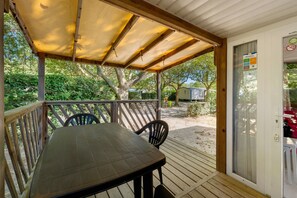 Un espacio de estar al aire libre cubierto con una mesa, sillas, una terraza de madera y vistas al entorno verde.