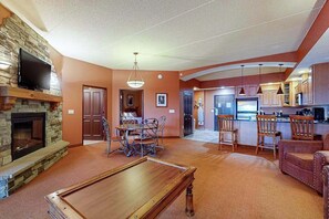 A living room with a pool table, a stone fireplace, and a television mounted on the wall.