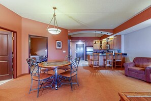 A dining area with a round table and chairs, a sofa, and a kitchen in the background.