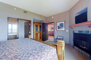 A hotel room with a large bed, a fireplace, a television, and a door leading to a balcony.