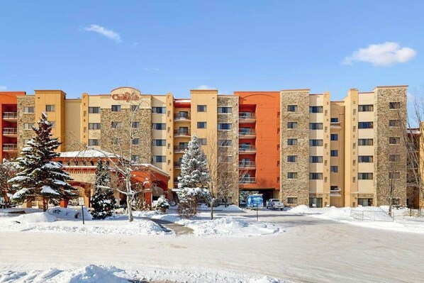 A multi-story hotel with a stone facade, balconies, and a parking area.