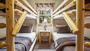 A cabin with two wooden bunk beds, a small table, and a window with a view of trees.