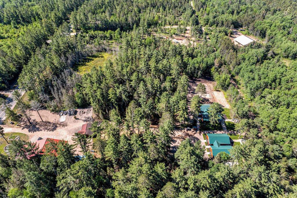 An aerial view of a forested area with a small building and a swimming pool.