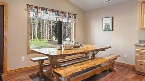 A wooden dining table with benches, a window with a view of trees, and a framed picture on the wall.