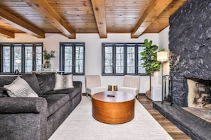 A living room with a stone fireplace, wooden ceiling beams, a round coffee table, and a sofa.