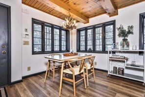 Un comedor con una mesa y sillas de madera, ventanas amplias y un candelabro.