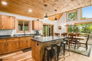 Una cocina con armarios de madera, una isla central, taburetes de bar y una mesa de comedor con sillas.