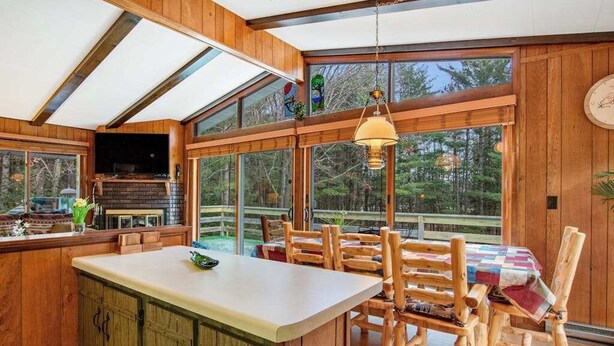 A wooden cabin interior with a kitchen, dining area, and large windows. - Lakefront Home with a Private Dock, Deck, Fireplace, Spacious Yard, & Playset (Eagle River)