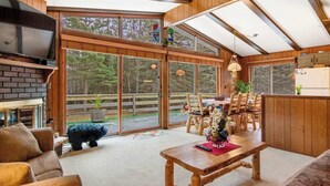 A spacious living area with a fireplace, wooden furniture, and large windows offering a view of the outdoors. - Lakefront Home with a Private Dock, Deck, Fireplace, Spacious Yard, & Playset (Eagle River)