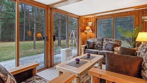 A cozy room with a wooden interior, large sliding glass doors, a sofa, a table, and a lamp. - Lakefront Home with a Private Dock, Deck, Fireplace, Spacious Yard, & Playset (Eagle River)