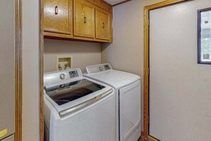 Un'area lavanderia con due lavatrici bianche, pensili in legno e una porta con finestra.