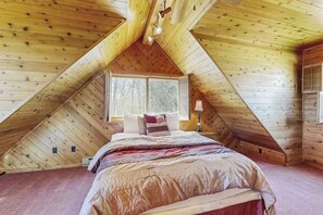 Ein Schlafzimmer mit schrägem Dach, einem Bett, einem Fenster und einer Lampe.