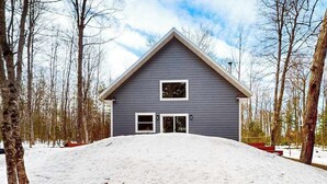 A house with a gabled roof, two windows, and a snow-covered front yard. - Lakefront home with, dock, kayaks, paddle boards, fire pit & more (Conover)