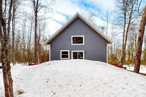 Una casa amb un teulat a dues aigües, dues finestres i un jardí davant cobert de neu.