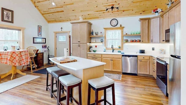 A kitchen with wooden ceiling, stainless steel appliances, and a central island with stools. - Lakefront home with, dock, kayaks, paddle boards, fire pit & more (Conover)