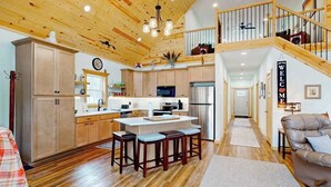 A spacious kitchen with wooden cabinets, a central island with stools, and a staircase leading to an upper level. - Lakefront home with, dock, kayaks, paddle boards, fire pit & more (Conover)
