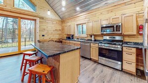 A modern kitchen with wooden walls, large windows, and a central island with stools. - Brand-new riverfront cabin with a open layout, gas grill, and W/D - dog-friendly (Tomahawk)