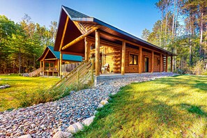 A log cabin with a covered porch, a staircase, and a gravel pathway.