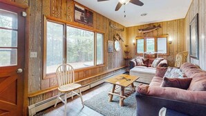 Ein Ferienhaus-Interieur mit Holzwänden, Deckenventilator, einer Couch, einem Tisch und großen Fenstern.