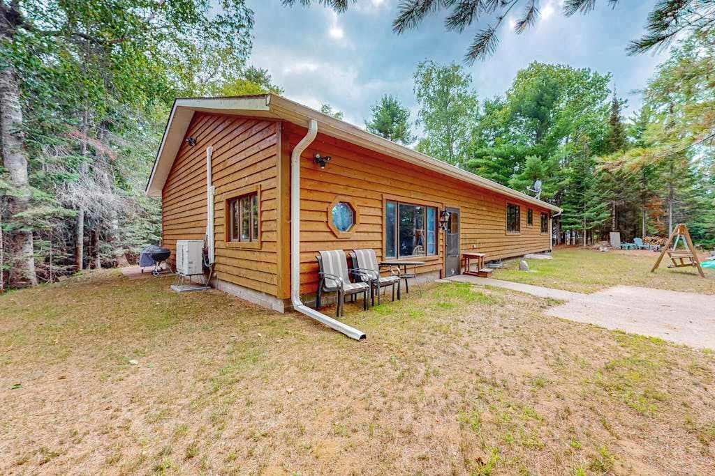 Une cabane en bois avec un porche, un barbecue et des meubles d’extérieur.