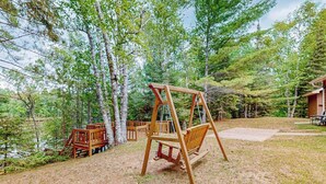 Ein Holzschaukelstuhl in einer bewaldeten Gegend, im Hintergrund eine Holzhütte.